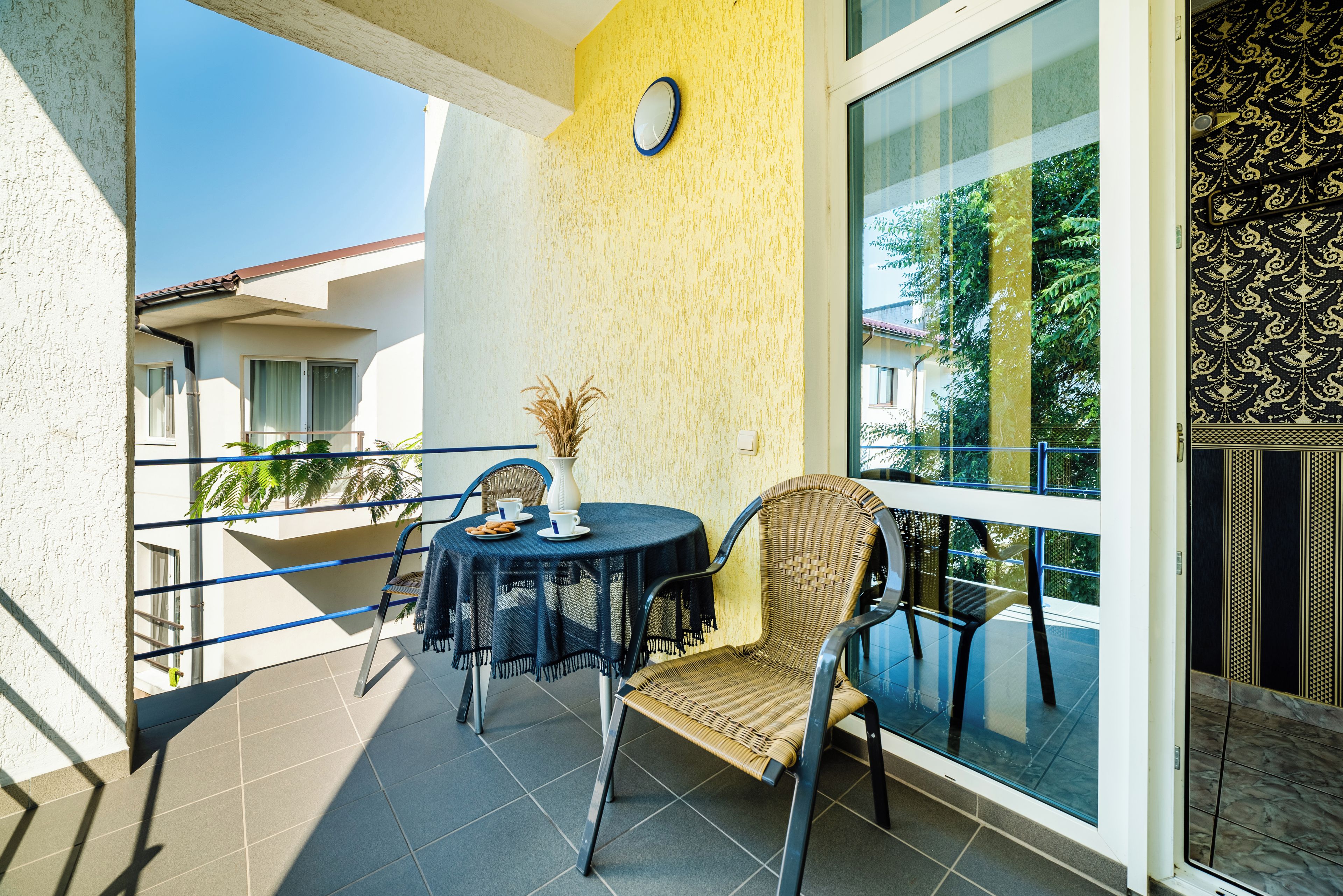 Ein Balkon mit rundem Tisch, Korbstühlen und einer Topfpflanze.