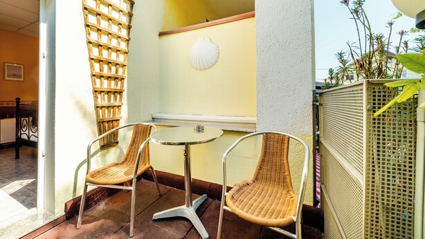 Un petit espace extérieur aménagé avec des chaises en osier et une table ronde, un treillage en bois et un décor mural en forme de coquillage blanc.
