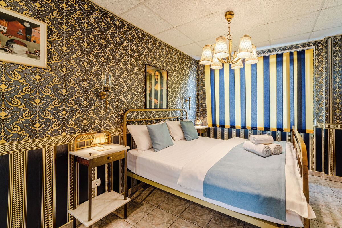 Een kamer met een bed, nachtkastje, lamp en een gestreept gordijn.
