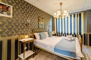 Een kamer met een bed, nachtkastje, lamp en een gestreept gordijn.