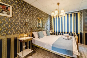 A room with a bed, bedside table, lamp, and a striped curtain.