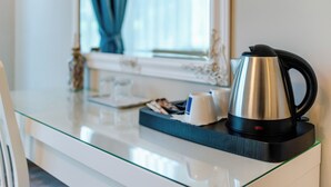 Une chambre d’hôtel moderne dotée d’un bureau avec un plateau en verre, d’une bouilloire en acier inoxydable, d’un plateau avec une tasse et un magazine, et d’une fenêtre avec des rideaux.