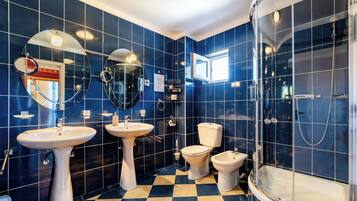 A bathroom with blue tiles, two sinks, a toilet, and a shower.