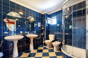 Un baño con azulejos azules, dos lavamanos, un inodoro y una ducha.