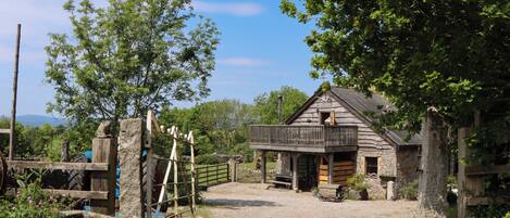A rustic wooden building with a balcony, surrounded by trees and a gravel path.