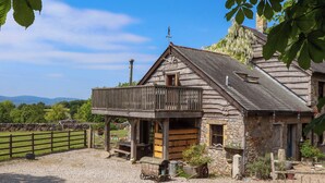 A rustic stone building with a wooden balcony, a chimney, and a stone wall in the background. - Buckleigh Lodge (Newton Abbot)