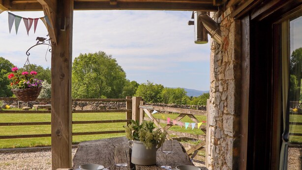 A rustic wooden table set for two with a view of a stone wall and greenery. - Buckleigh Lodge (Newton Abbot)