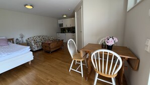 A compact room with a bed, a sofa, a dining table with chairs, a small kitchen area, and a window. - Annex for rent – ​​Near Mallboden and Lokverkstaden in beautiful Motala |SE10023 (Motala)