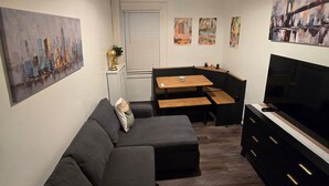 A living room with a dark-colored sofa, a wooden dining table, a black TV stand, and a ceiling fan. - Two bedroom  in United States of America, Jersey City (Jersey City)