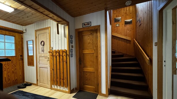 Un interior de madera con una escalera, una puerta decorada con un adorno y un perchero.