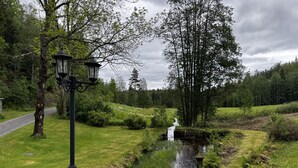 Paisaje rural con un arroyo, árboles y un farol.