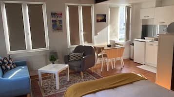 Ein gemütlicher Wohnbereich mit Sofa, einem kleinen Tisch, einem Sessel, einem Bett, einem Schreibtisch und einer Küchenzeile.