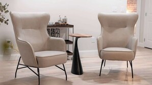 Duas poltronas bege com pés de metal preto, uma mesinha redonda e um aparelho de ar condicionado na parede.
