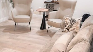 Uma sala de estar moderna com um sofá bege, duas poltronas e uma mesa redonda pequena.