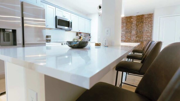 Una cocina moderna con armarios blancos, electrodomésticos de acero inoxidable y una isla central con asientos.