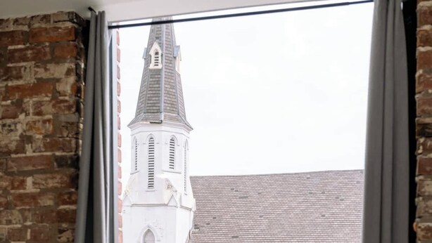 A room with a bed, a window with curtains, and a view of a church with a tall steeple. - NEW in Downtown + free parking (Lexington)
