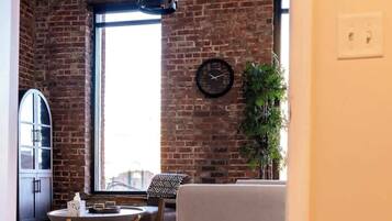 A modern living room with exposed brick walls, a large window, a round dining table, and a sofa.
