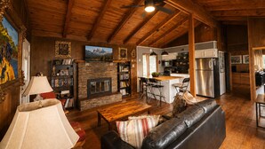 A spacious living area with a fireplace, a kitchen in the background, and a ceiling fan.