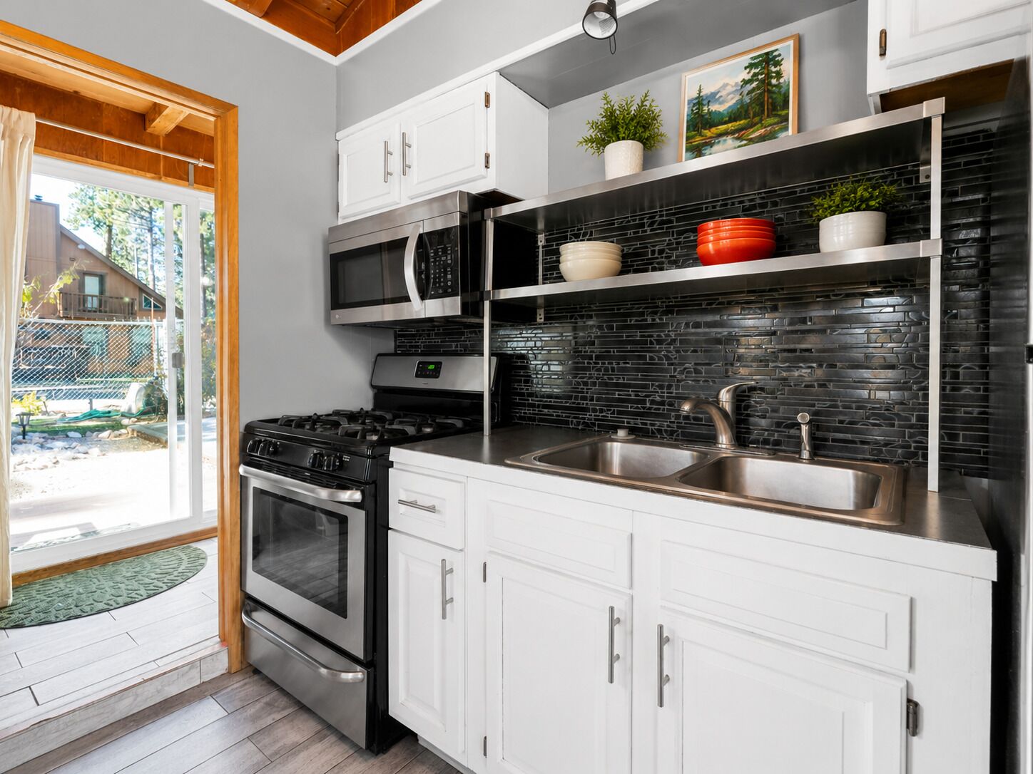 A modern kitchen with white cabinetry, a stainless steel stove, a microwave, and a black tiled backsplash.