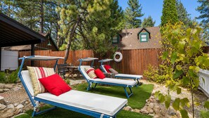 A backyard with two sun loungers, a wooden fence, and a house with a chimney.