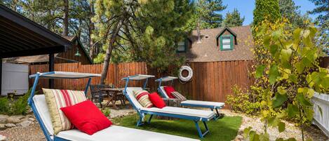 A backyard with two sun loungers, a wooden fence, and a house with a chimney.