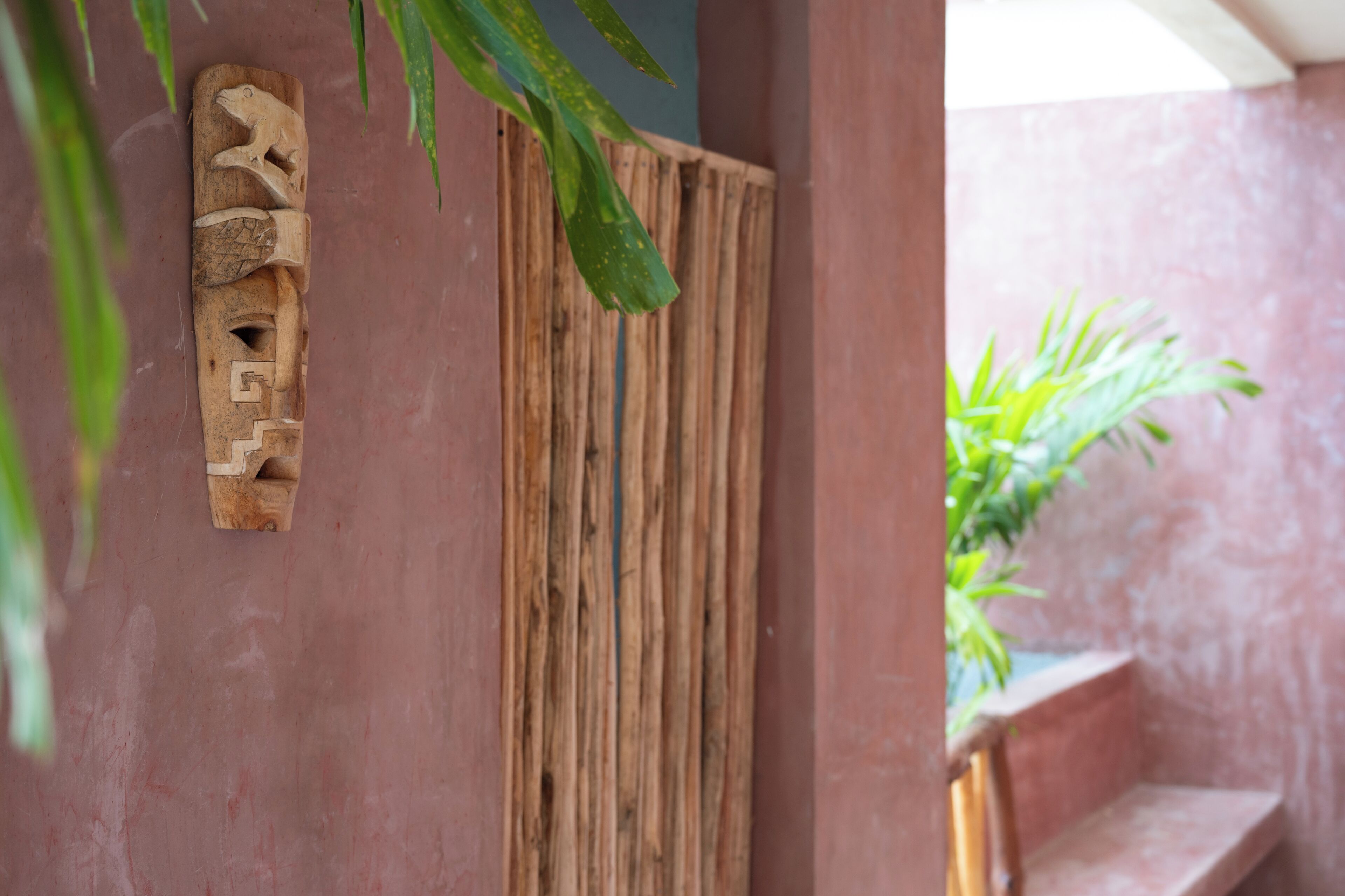 Un panel de madera con diseño de rana tallada, un revestimiento de listones verticales de madera y una escalera que lleva a un balcón con una planta.