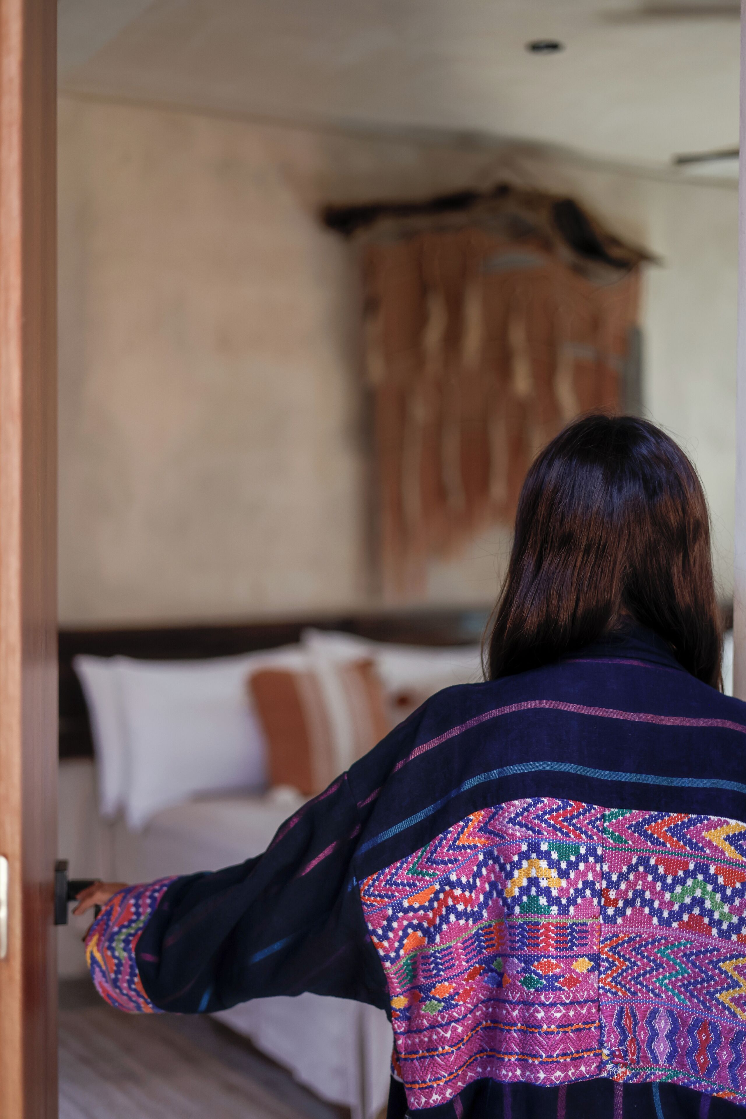 A person standing at a doorway, facing a bed with white linens and a wooden headboard.