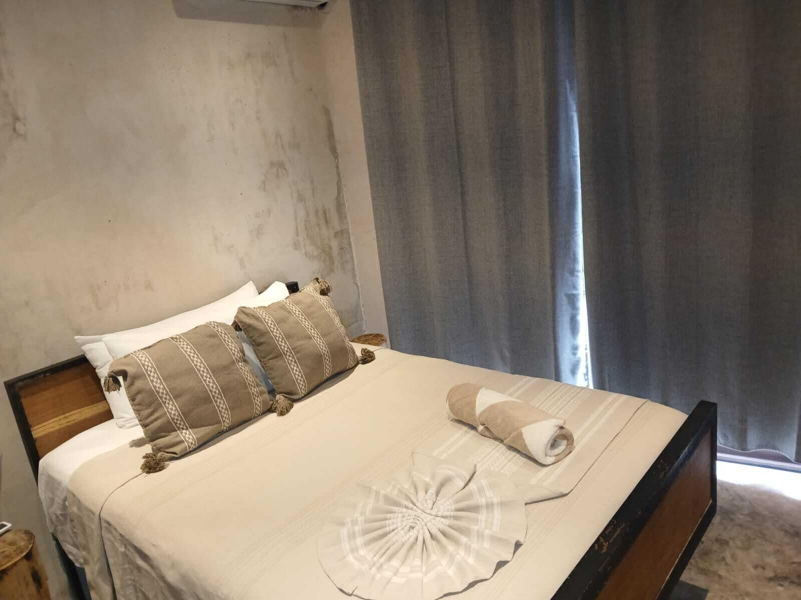 Un lit bien fait, recouvert d’une couverture blanche et beige, agrémenté de deux coussins décoratifs et d’une serviette enroulée.