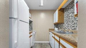 Una cocina estrecha con gabinetes blancos, encimera de granito y salpicadero de azulejos.