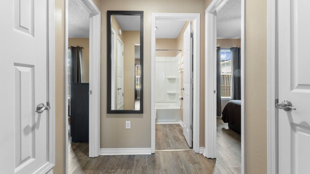 Un pasillo con un espejo, una puerta que da al baño y una habitación visible a través de una puerta abierta.