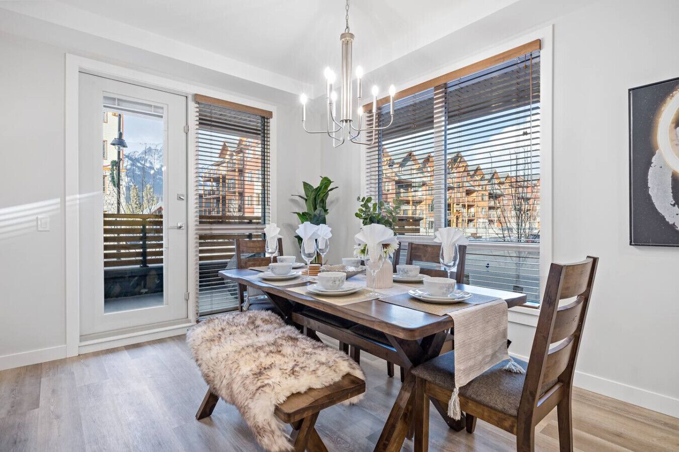 A dining area with a wooden table set for four, a chandelier, and a bench with a fur throw.