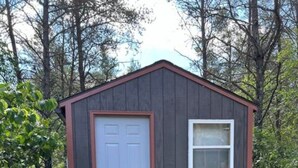A small, single-story shed with a white door and a window, surrounded by trees and grass. - Cozy Northwoods property (Crivitz)