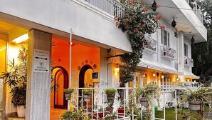 A hotel entrance with a warm orange facade, a sign indicating 'The B&B World Reception', and a well-maintained garden with potted plants. - J Startup House (Jaipur)