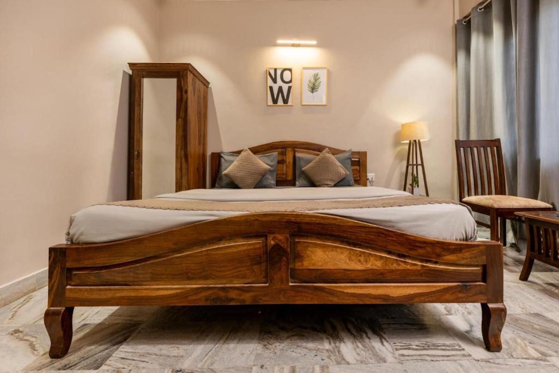 A wooden bed with a headboard, a bedside table, and a chair. There are two framed pictures on the wall.