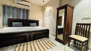 A bedroom with a bed, a wooden chair, a mirror, and an air conditioning unit. - J Startup House (Jaipur)