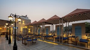 An outdoor dining area with tables and chairs, covered by umbrellas, and street lamps. - J Startup House (Jaipur)