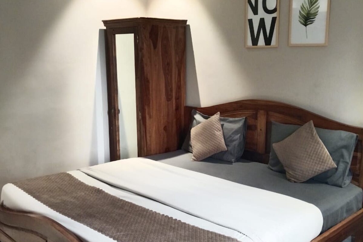 A bedroom with a wooden bed frame, a large bedspread, and a striped rug.