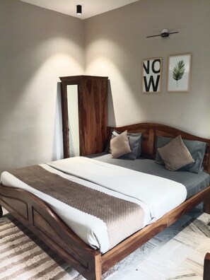 A bedroom with a wooden bed frame, a large bedspread, and a striped rug. - J Startup House (Jaipur)