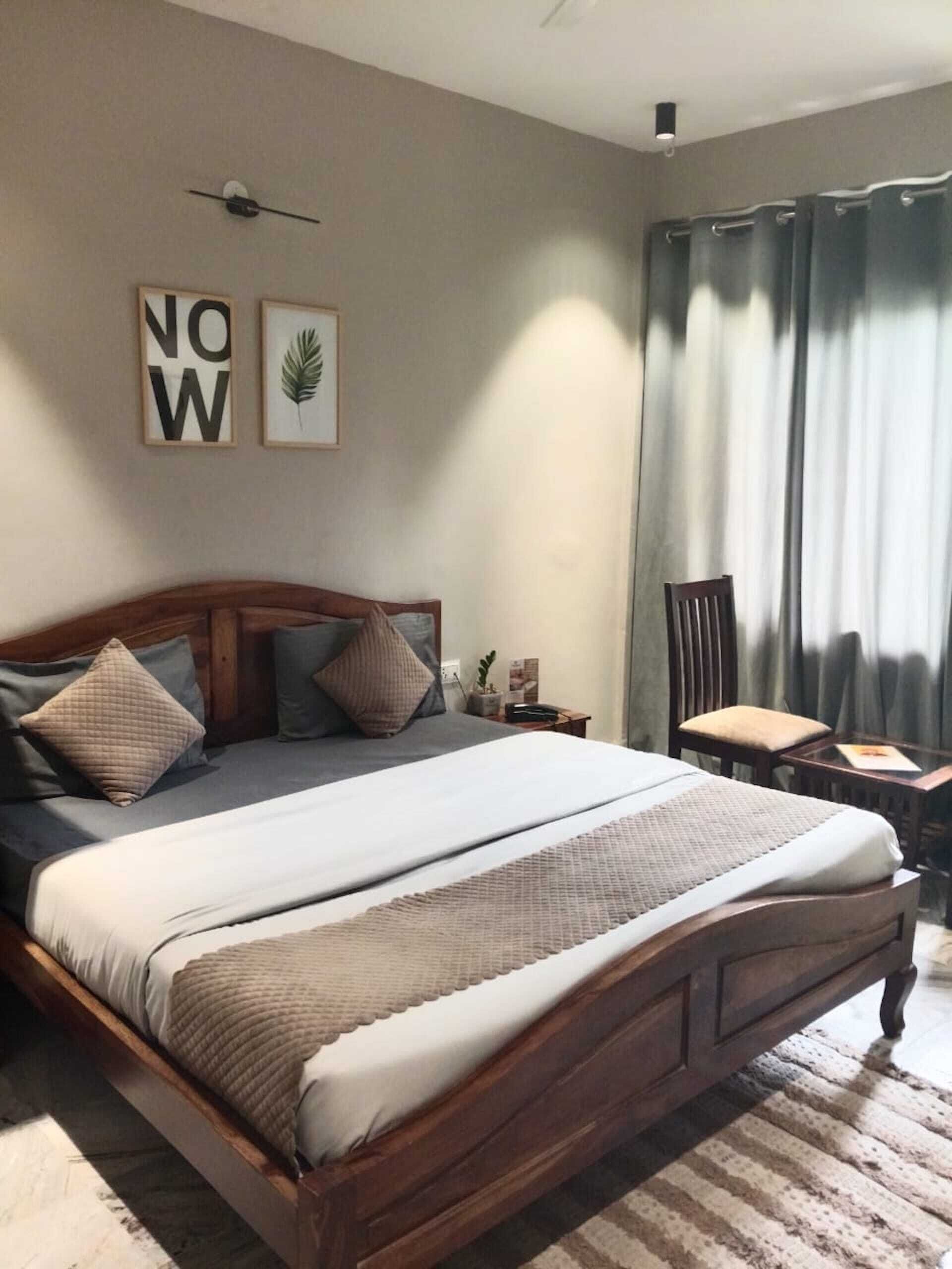 A neatly arranged bedroom with a wooden bed, a small bedside table, a chair, and a window with curtains.