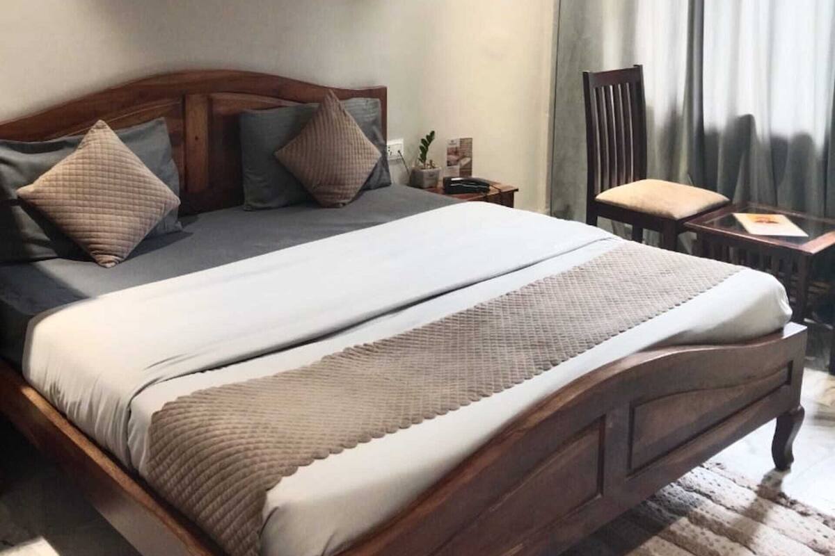 A neatly arranged bedroom with a wooden bed, a small bedside table, a chair, and a window with curtains.