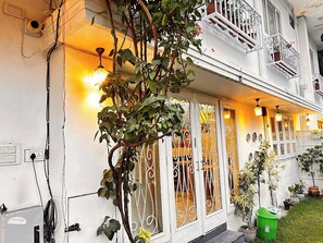 A white building with a balcony, a garden, and a green trash bin. - J Startup House (Jaipur)
