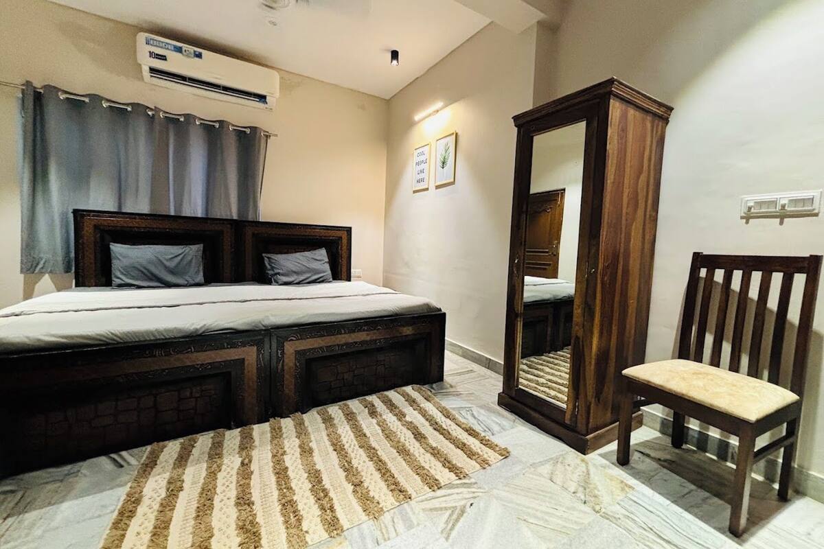 A bedroom with a bed, a wooden chair, a mirror, and an air conditioning unit.