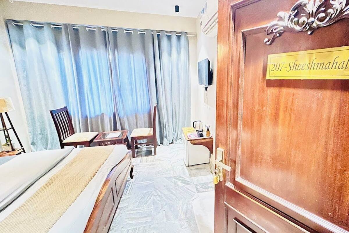 A hotel room with a bed, a desk, a chair, and a wooden door with a sign.