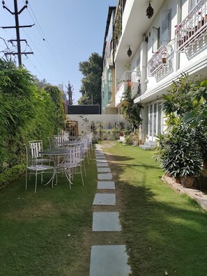 Une cour intérieure avec une table et des chaises, entourée d’une végétation luxuriante et bordée d’un chemin en pierre.