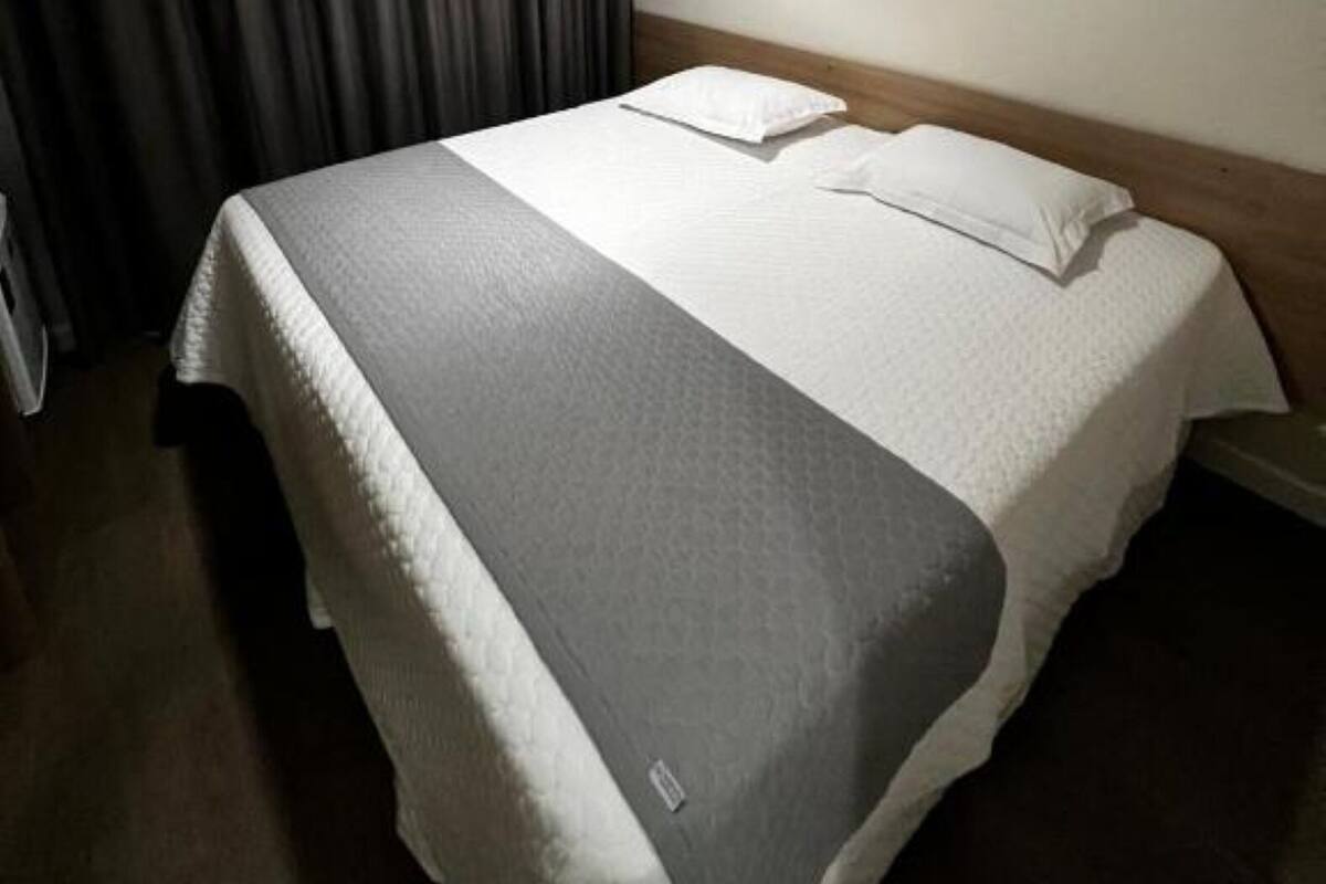 Une chambre d’hôtel avec un lit, une table de chevet, une lampe et une fenêtre avec des rideaux.