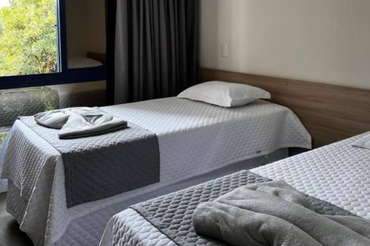 Une chambre d’hôtel avec deux lits, une grande fenêtre et une vue sur la verdure environnante.