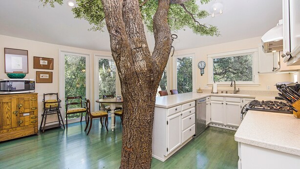 Una cocina con un gran tronco de árbol como pieza central, armarios de madera, un microondas y un fregadero.