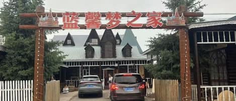 A gated entrance with a sign above, two cars parked in front, and a building with a distinctive roofline.
