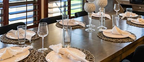 A dining table set with plates, glasses, and napkins, with a view of a building through the window.