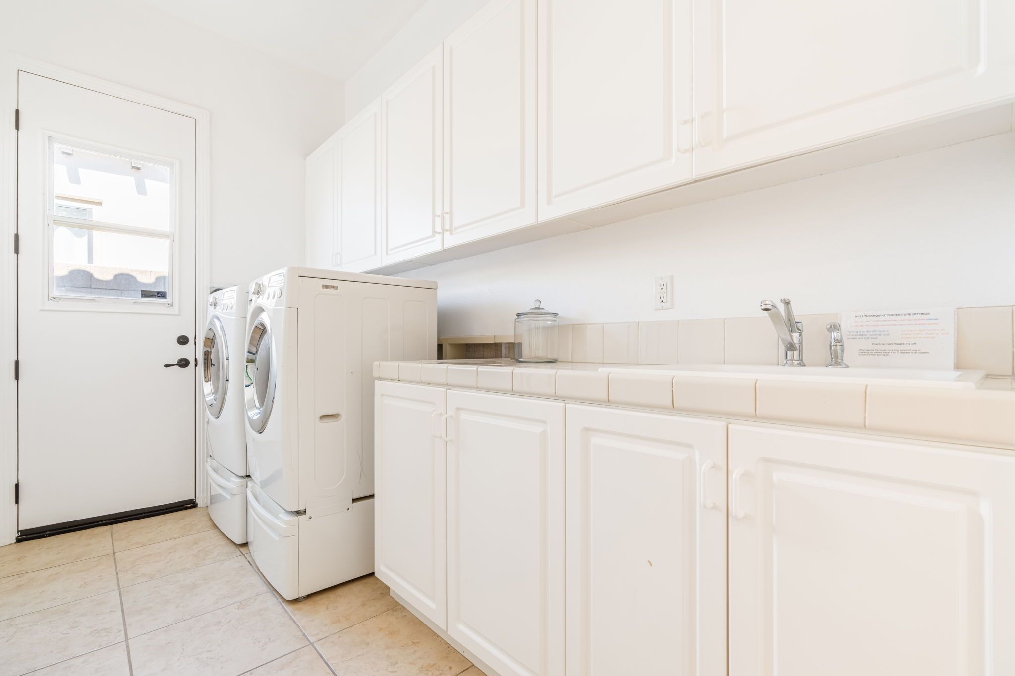 A clean, white kitchen with a built-in washer and dryer, a tiled backsplash, and white cabinetry.
